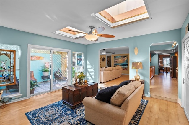 living room with a skylight, ceiling fan, and light hardwood / wood-style floors