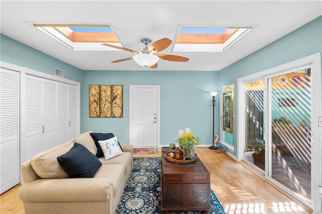 living room with a skylight, ceiling fan, and light hardwood / wood-style floors