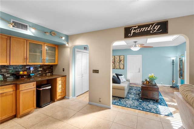 kitchen with light tile patterned floors, tasteful backsplash, ceiling fan, and dark stone countertops