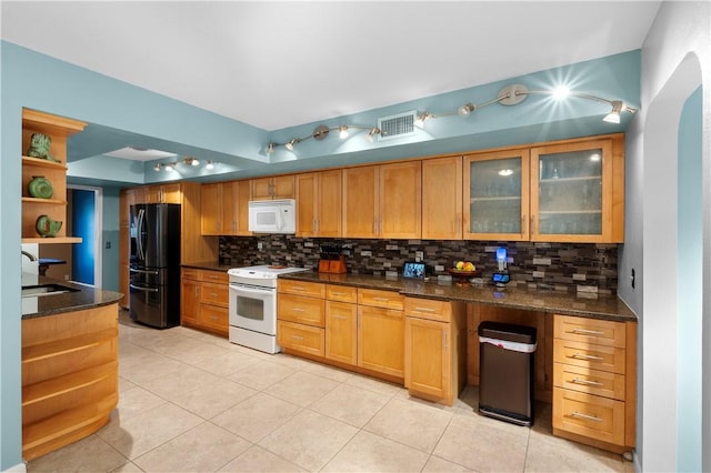 kitchen with sink, light tile patterned flooring, dark stone counters, and white appliances