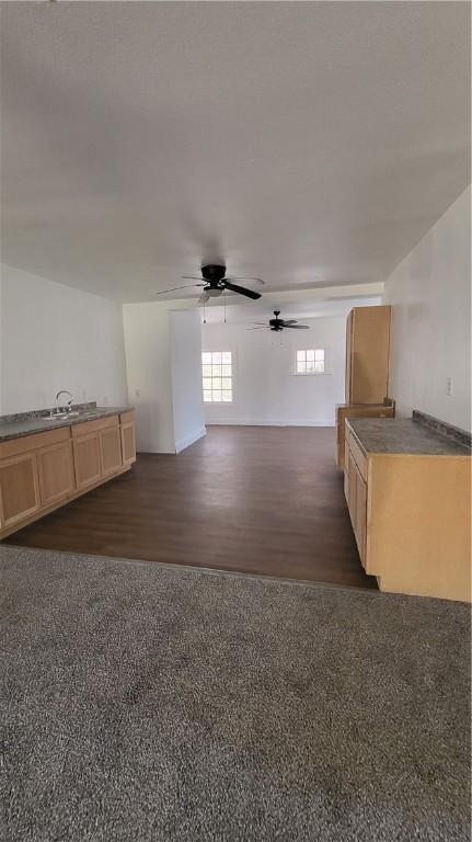 unfurnished living room featuring dark wood-type flooring and ceiling fan