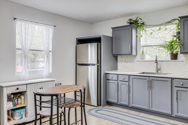 kitchen featuring light wood-type flooring, tasteful backsplash, sink, gray cabinets, and stainless steel refrigerator