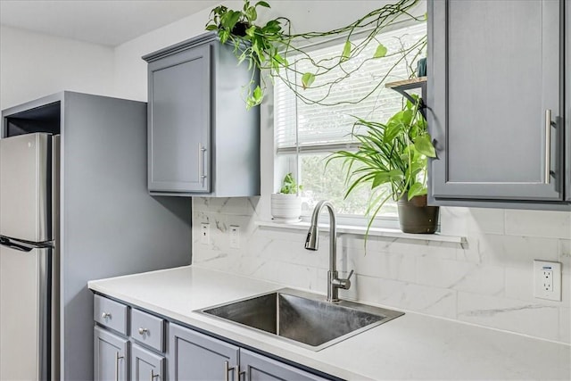 kitchen with gray cabinets, stainless steel fridge, sink, and decorative backsplash