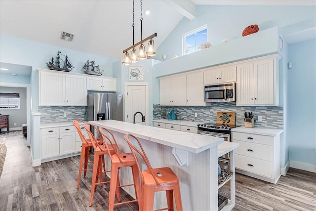 kitchen featuring a kitchen bar, white cabinetry, high vaulted ceiling, a center island with sink, and appliances with stainless steel finishes