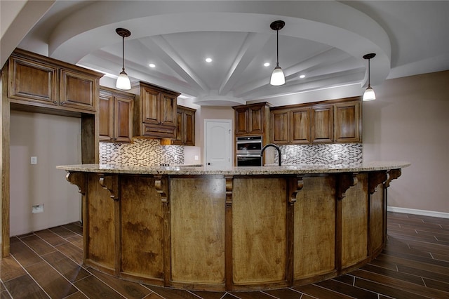 kitchen featuring hanging light fixtures, tasteful backsplash, light stone counters, a large island with sink, and a breakfast bar