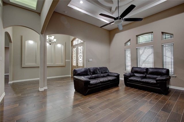 living room with a towering ceiling, ceiling fan with notable chandelier, and dark wood-type flooring