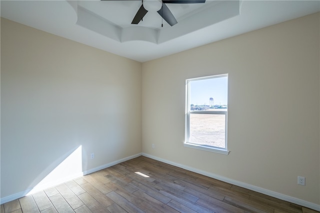 spare room with a tray ceiling, ceiling fan, and light hardwood / wood-style floors