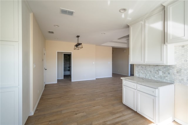 kitchen featuring tasteful backsplash, light stone counters, decorative light fixtures, white cabinets, and light hardwood / wood-style floors