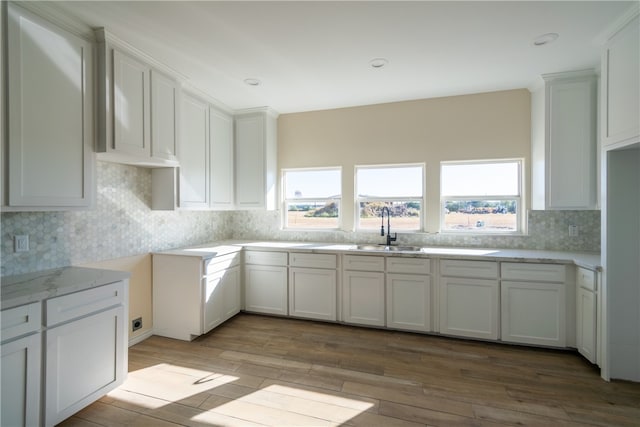 kitchen with decorative backsplash, white cabinetry, light hardwood / wood-style flooring, and sink