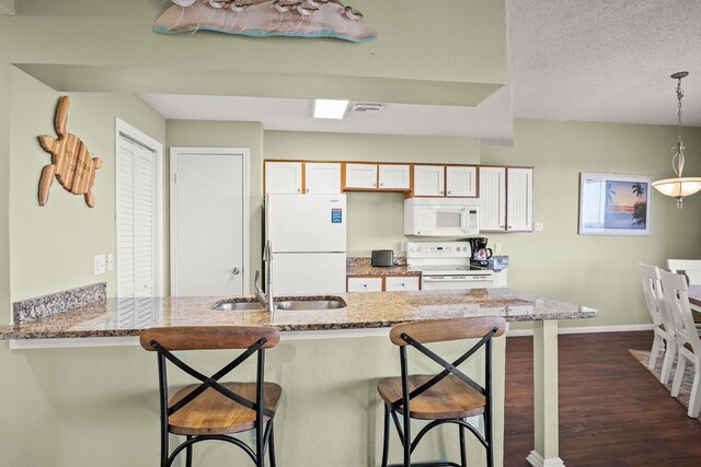 kitchen with white appliances, dark hardwood / wood-style floors, sink, a breakfast bar area, and kitchen peninsula