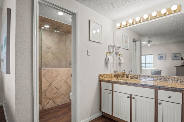 bathroom featuring ceiling fan, a textured ceiling, wood-type flooring, vanity, and tiled shower