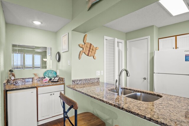 kitchen featuring white cabinetry, white refrigerator, dark hardwood / wood-style floors, light stone countertops, and sink