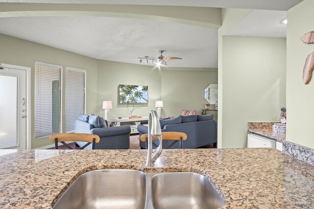 kitchen featuring sink, light stone counters, ceiling fan, and a textured ceiling