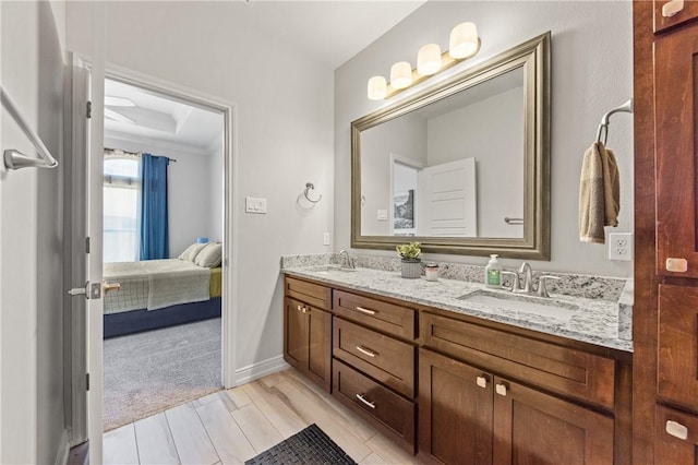 ensuite bathroom with double vanity, wood finish floors, and baseboards