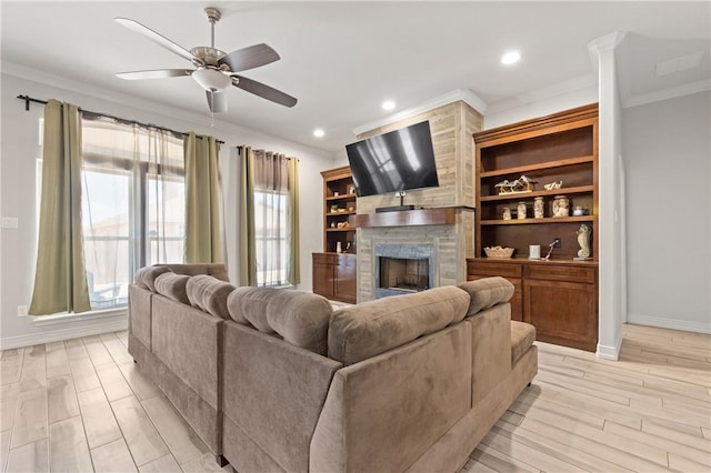 living room featuring crown molding, baseboards, a large fireplace, ceiling fan, and light wood-style flooring