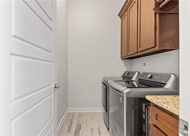 washroom featuring cabinet space, washing machine and clothes dryer, baseboards, and light wood finished floors