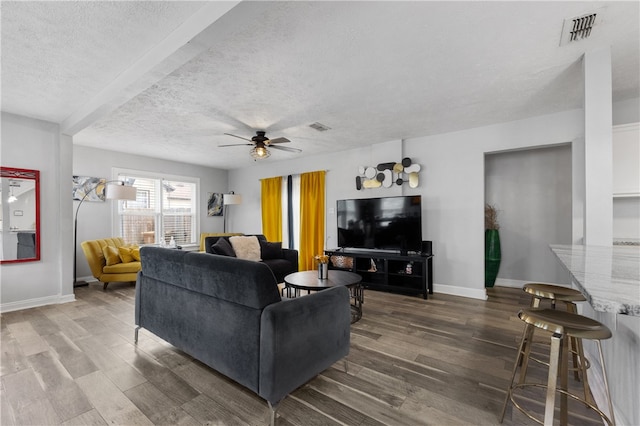 living room featuring dark hardwood / wood-style flooring, a textured ceiling, ceiling fan, and beam ceiling