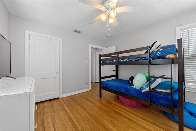 bedroom with a textured ceiling, ceiling fan, and light hardwood / wood-style flooring