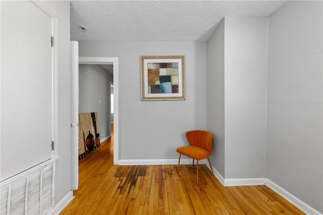 hallway with a textured ceiling and light hardwood / wood-style flooring