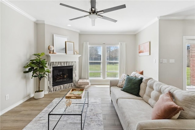 living area with a glass covered fireplace, ornamental molding, baseboards, and wood finished floors