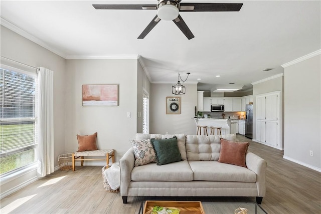 living area with baseboards, a ceiling fan, light wood-style floors, and ornamental molding