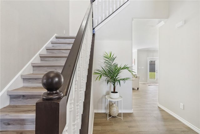 stairway featuring a towering ceiling, baseboards, and wood finished floors