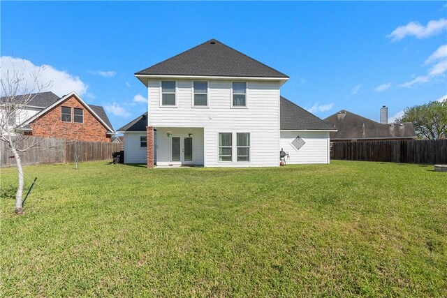 rear view of property featuring a yard, a fenced backyard, french doors, and roof with shingles