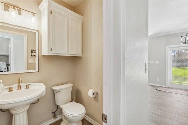 half bath with toilet, wood finished floors, baseboards, and a sink