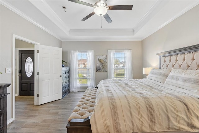 bedroom with a ceiling fan, a tray ceiling, wood finished floors, and ornamental molding