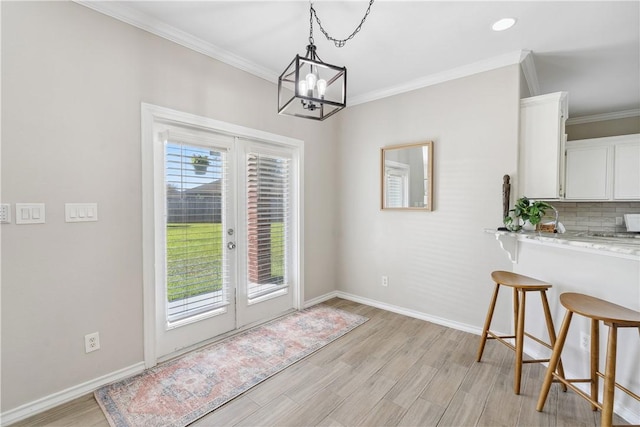 dining space featuring light wood-type flooring, ornamental molding, french doors, baseboards, and a chandelier