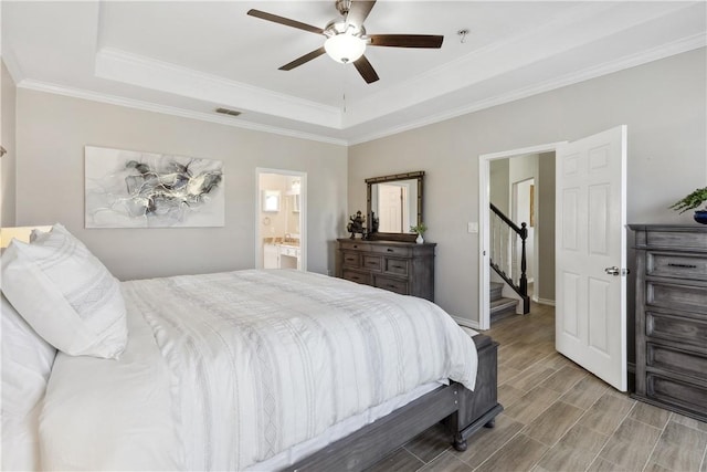 bedroom featuring visible vents, wood finish floors, ceiling fan, a tray ceiling, and ensuite bath