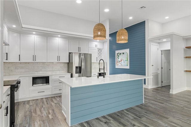 kitchen featuring white cabinets, pendant lighting, stainless steel appliances, and an island with sink