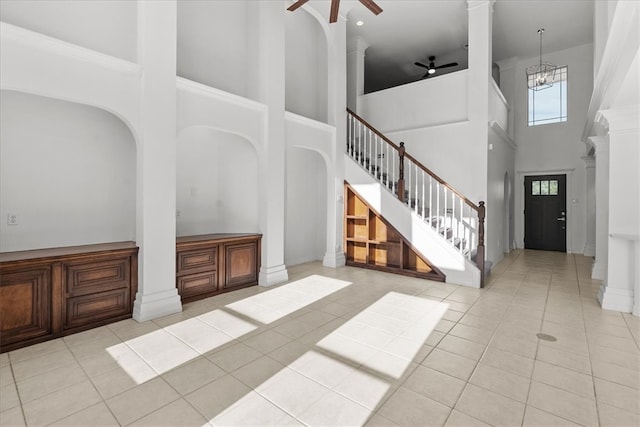 entrance foyer with ornate columns, ceiling fan with notable chandelier, light tile patterned floors, and a high ceiling