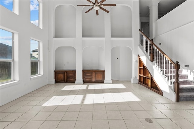 unfurnished living room with a towering ceiling, ceiling fan, light tile patterned floors, and decorative columns