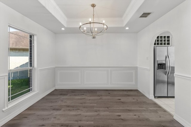 unfurnished dining area with an inviting chandelier, hardwood / wood-style floors, ornamental molding, and a raised ceiling