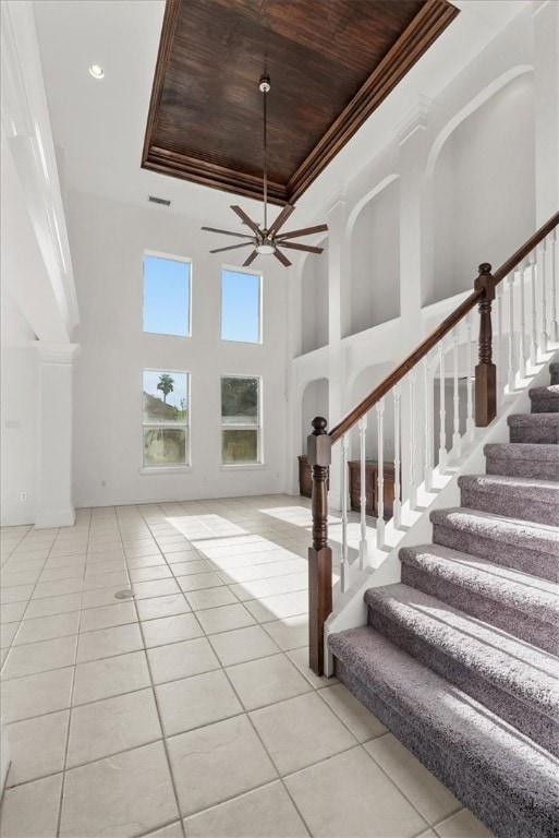 tiled entrance foyer with ceiling fan, a towering ceiling, wood ceiling, a raised ceiling, and crown molding