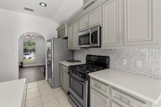 kitchen featuring appliances with stainless steel finishes, backsplash, light hardwood / wood-style flooring, lofted ceiling, and a notable chandelier