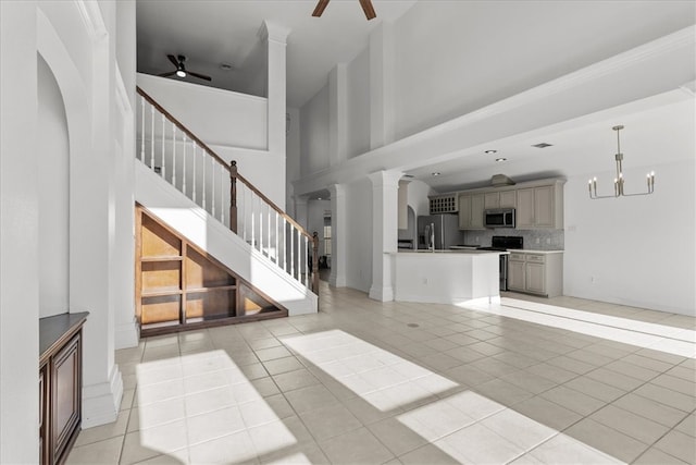 unfurnished living room with ceiling fan with notable chandelier, light tile patterned flooring, a high ceiling, and decorative columns