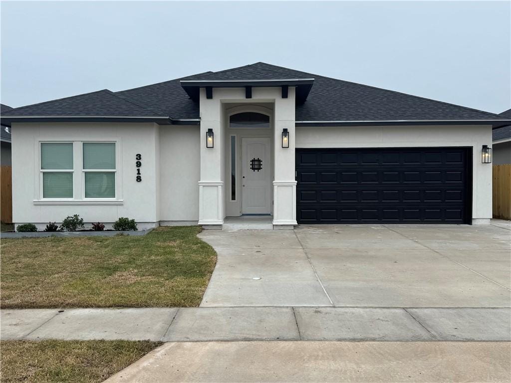 prairie-style home featuring an attached garage, driveway, roof with shingles, stucco siding, and a front lawn