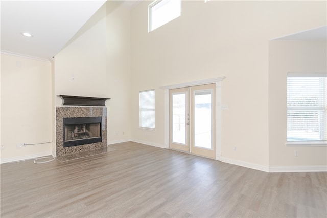 unfurnished living room featuring a tile fireplace, high vaulted ceiling, and light wood-type flooring