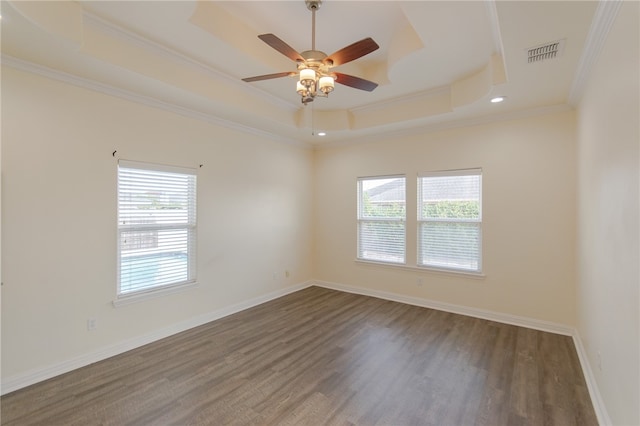 empty room with a tray ceiling, a wealth of natural light, crown molding, and dark hardwood / wood-style floors