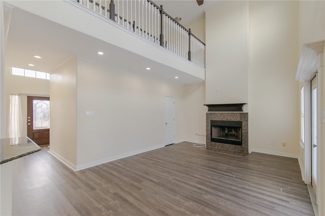 unfurnished living room featuring a tiled fireplace, a high ceiling, and hardwood / wood-style flooring