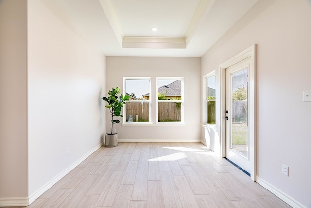 interior space with a raised ceiling, crown molding, light wood-style flooring, and baseboards