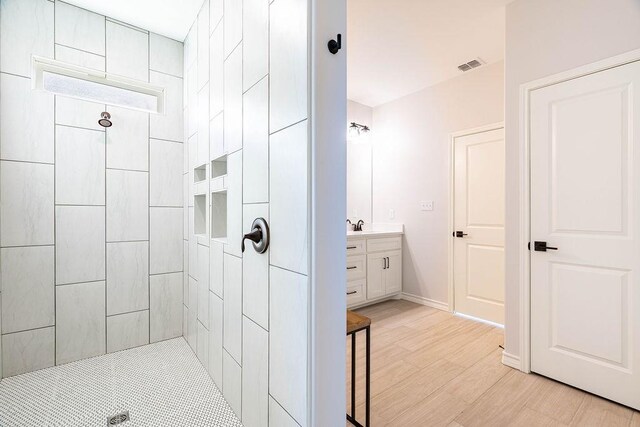 full bath featuring vanity, wood finished floors, a tile shower, and visible vents