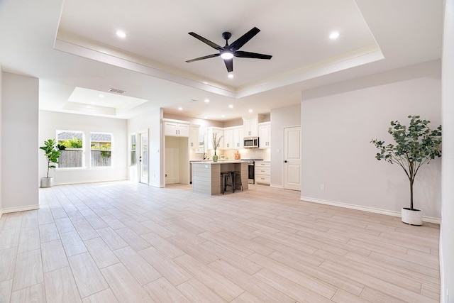 unfurnished living room featuring a raised ceiling, ceiling fan, and light wood-type flooring