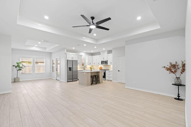 unfurnished living room featuring light wood-type flooring, baseboards, and a raised ceiling