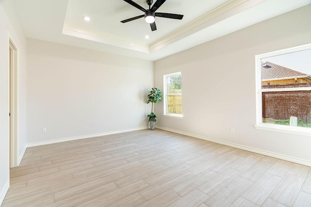 empty room with light wood-type flooring, a raised ceiling, baseboards, and recessed lighting