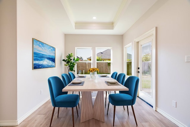 dining space with crown molding, a tray ceiling, light wood-style floors, and baseboards