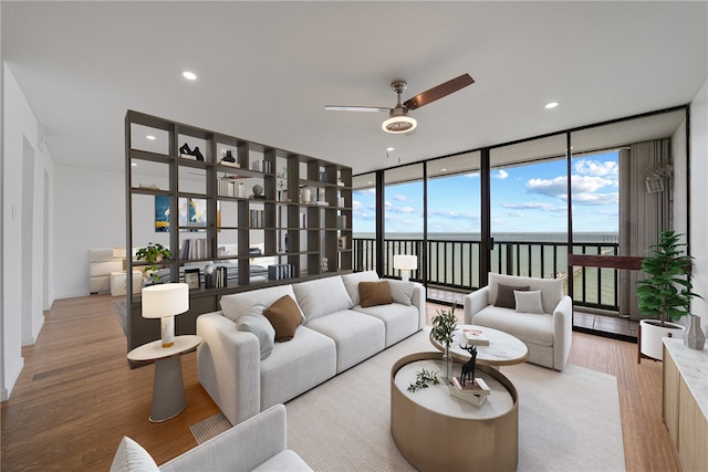 living room with expansive windows, light hardwood / wood-style floors, ceiling fan, and a water view