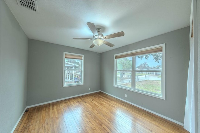 unfurnished room with a healthy amount of sunlight, visible vents, light wood-style flooring, and baseboards